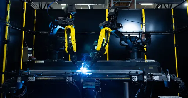 Två maskiner svetsar i en mörk produktionshall