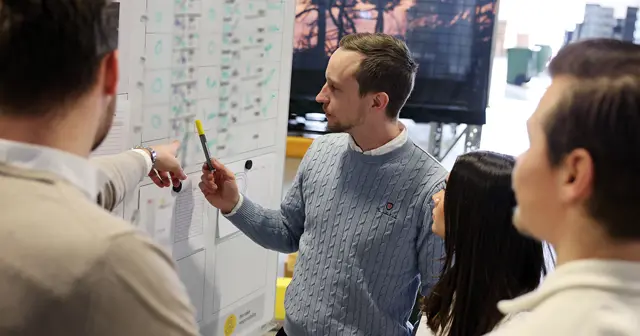 En man håller presentation vid en tavla för tre anställda om produktionsteknik